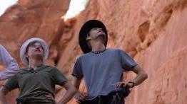 two students 和 their professor look up into a canyon