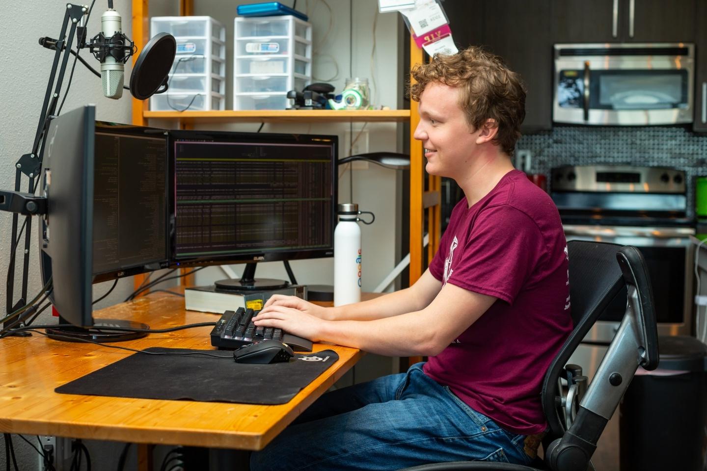 person sitting at desk in front of three computer screens