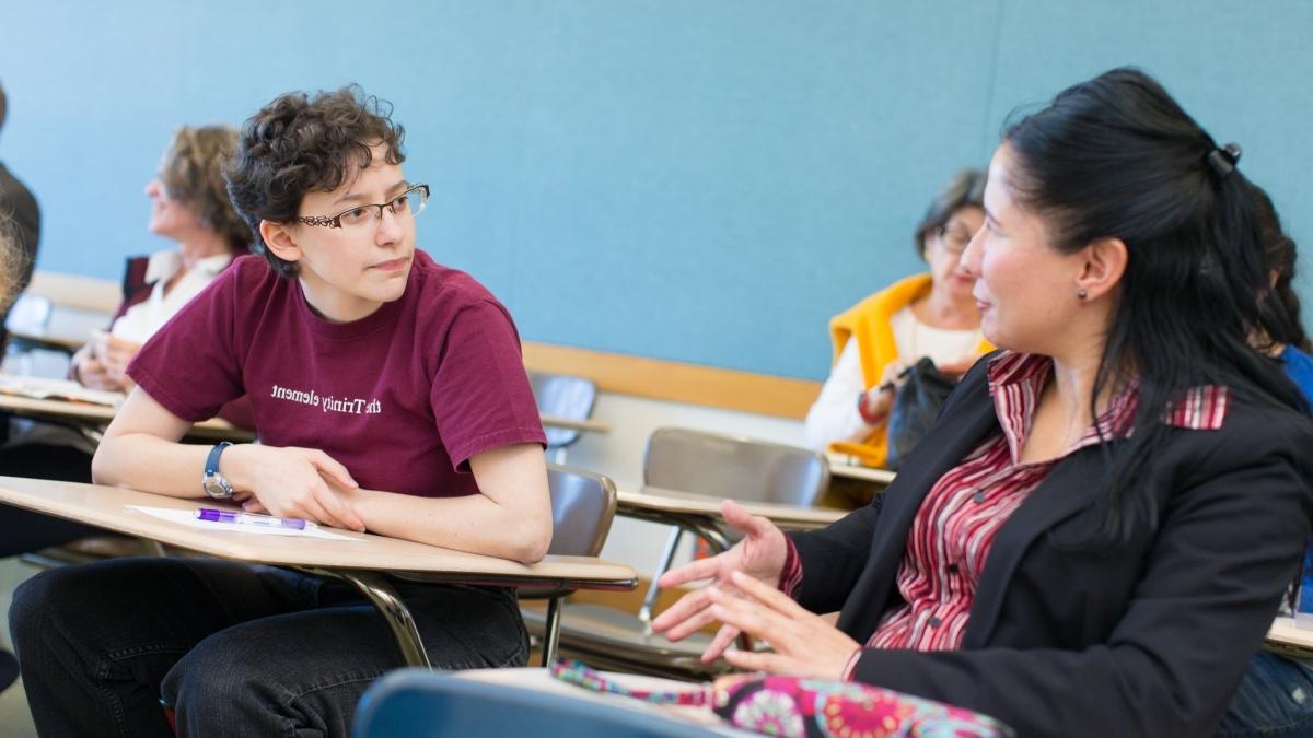 Two students sitting in desks talking